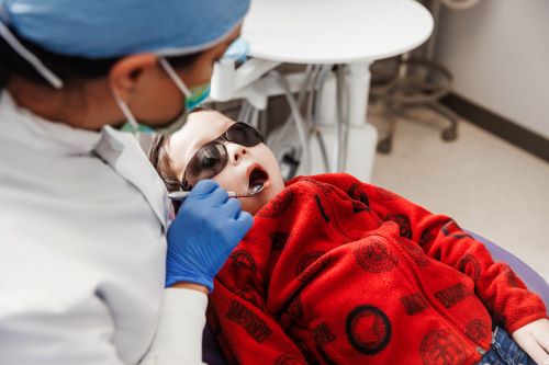 Child in dental chair gets his teeth examined by dental hygienist
