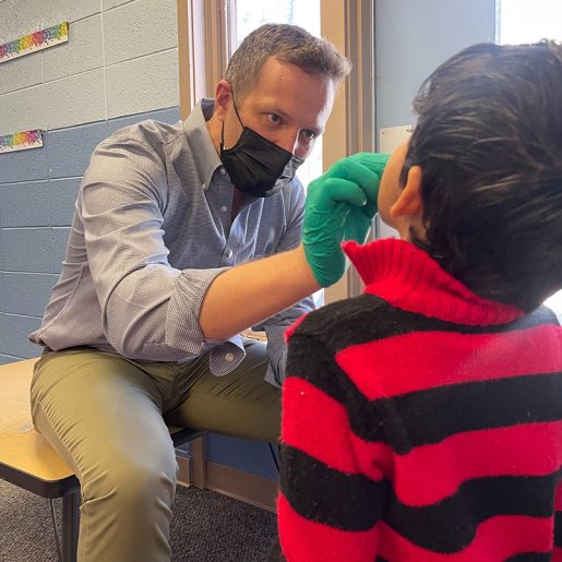 Image of dentist applying fluoride varnish to boy's teeth while at school