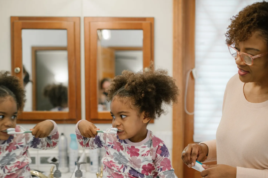Child brushes teeth in the mirror while female relative watches